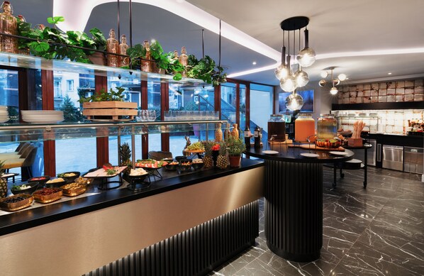 A modern hotel lobby with a glass partition displaying a buffet, a large potted plant, and a view of the cityscape.