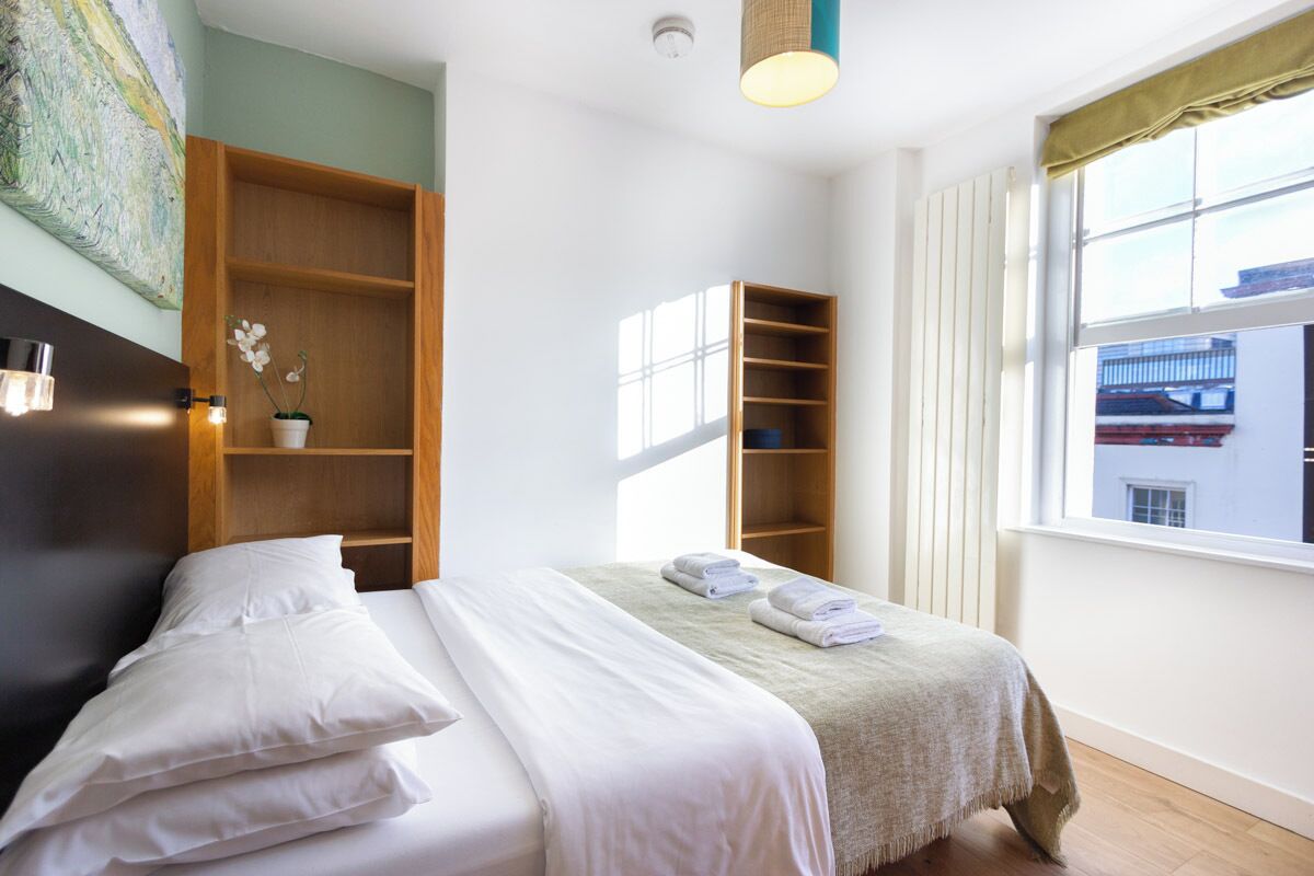 Een hotelkamer met een bed, een houten plankunit, een raam met gordijnen en een plafondlamp.
