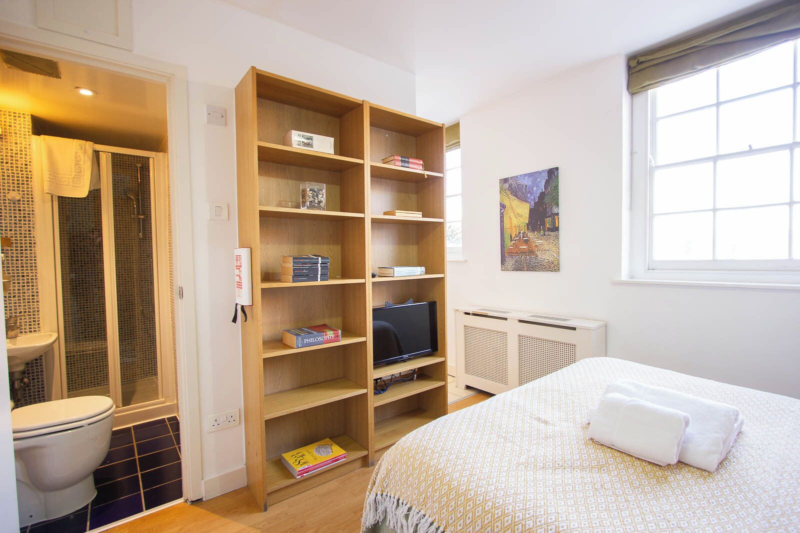 A bedroom with a bed, a TV, a bookshelf, and a shower area.