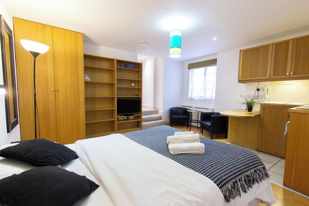 A hotel room with a bed, a desk, a chair, a wardrobe, and a kitchenette.