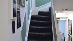 A staircase with a carpeted floor, white walls, and green wainscoting. There are framed pictures on the walls and a sign indicating office locations.