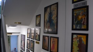 A hallway with multiple framed artworks on the walls, a small table with books, and a sign indicating office locations.