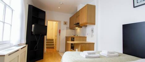 A hotel room with a bed, a desk, a kitchenette, and a bathroom.