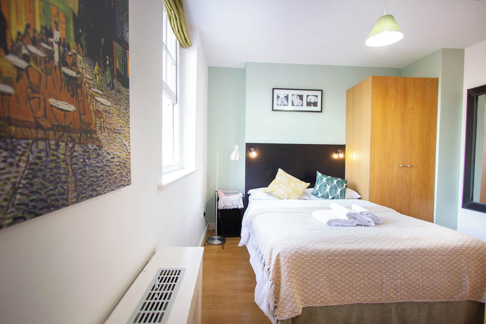 Ein Hotelzimmer mit Bett, Nachttisch, Lampe, Schrank und einem Bild an der Wand.