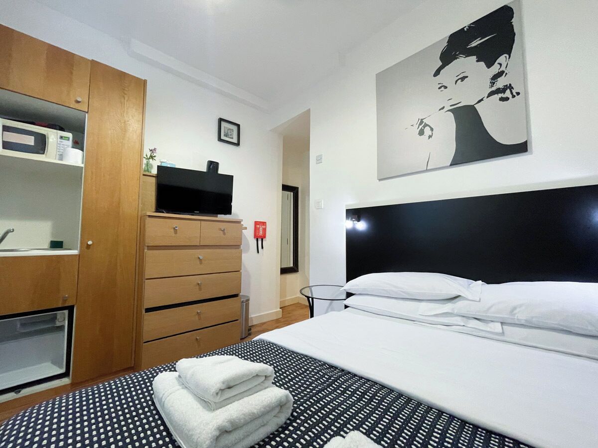 A hotel room with a bed, a wooden wardrobe, a television, and a painting on the wall.