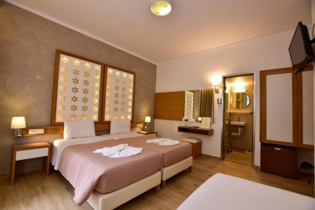 A hotel room with two beds, a wooden headboard, a bedside table with a lamp, a mirror, a small bathroom, and a television.