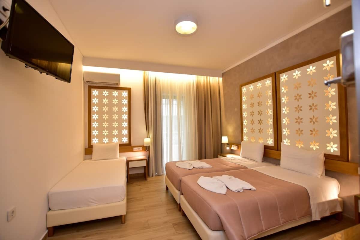 Een hotelkamer met twee bedden, een televisie, een raam met gordijnen en decoratieve lichtpanelen.