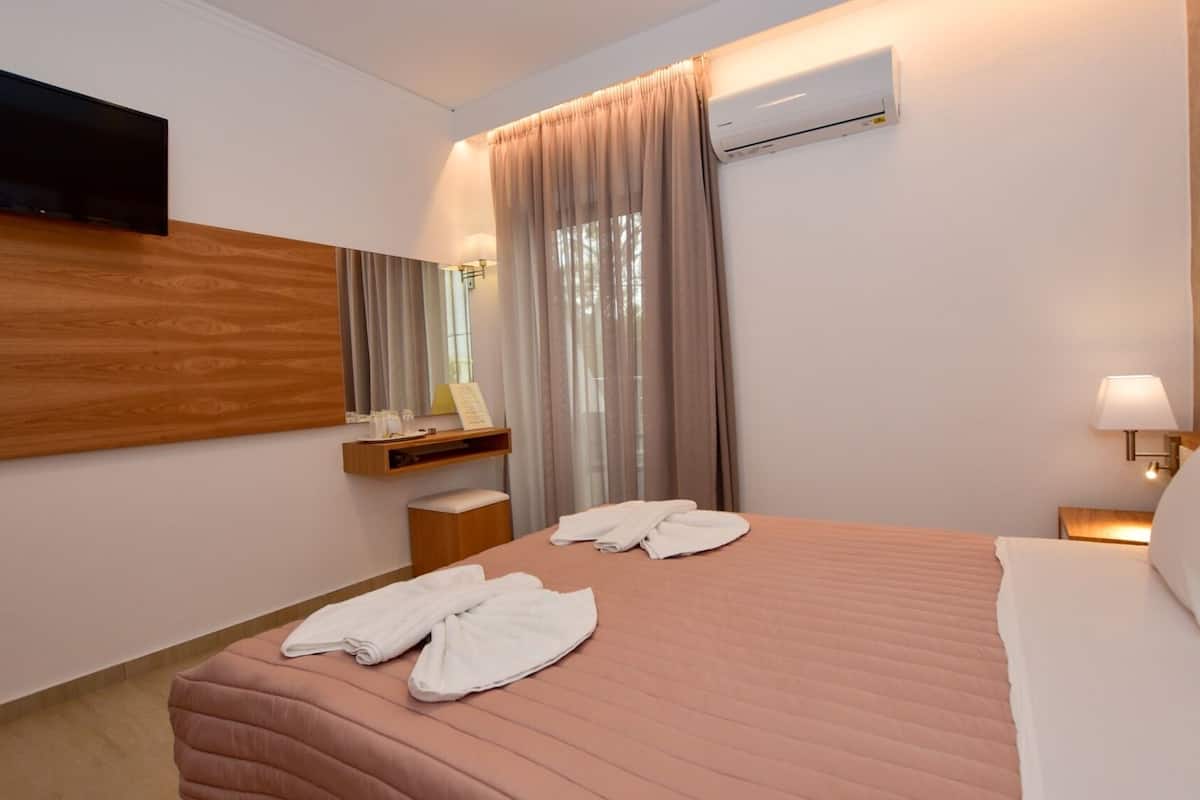 Een hotelkamer met een bed, een flatscreen televisie aan de muur, een nachtkastje met een lamp en een airconditioner.