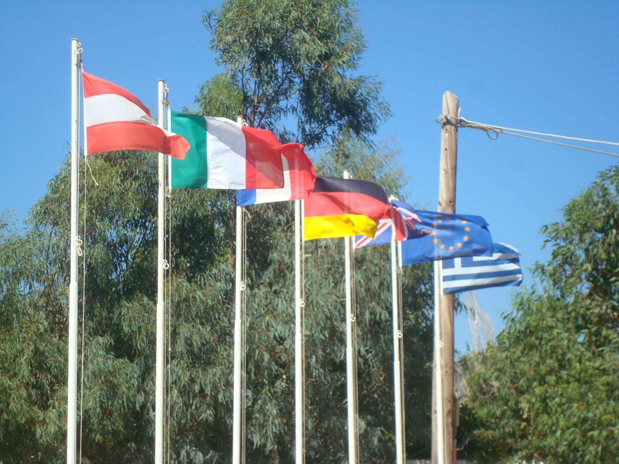 Una hilera de banderas en mástiles, entre ellas las de Italia, Alemania y la Unión Europea.