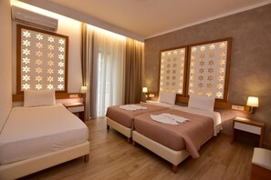 A hotel room with two beds, a sitting area, and a large window with curtains.