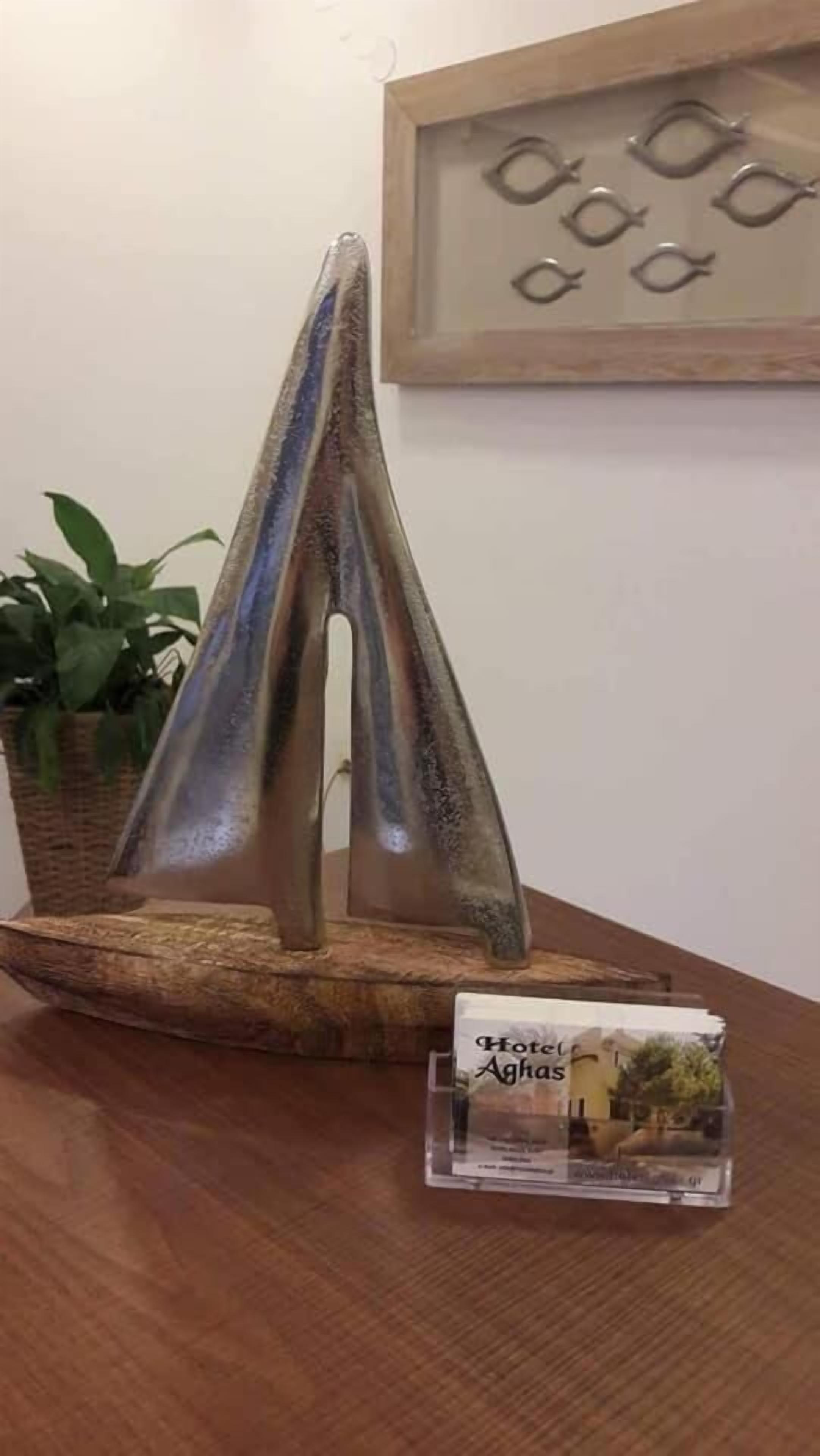 Mesa de madeira com uma escultura decorativa de barco à vela, uma obra de arte emoldurada e um folheto do Hotel Aghas.