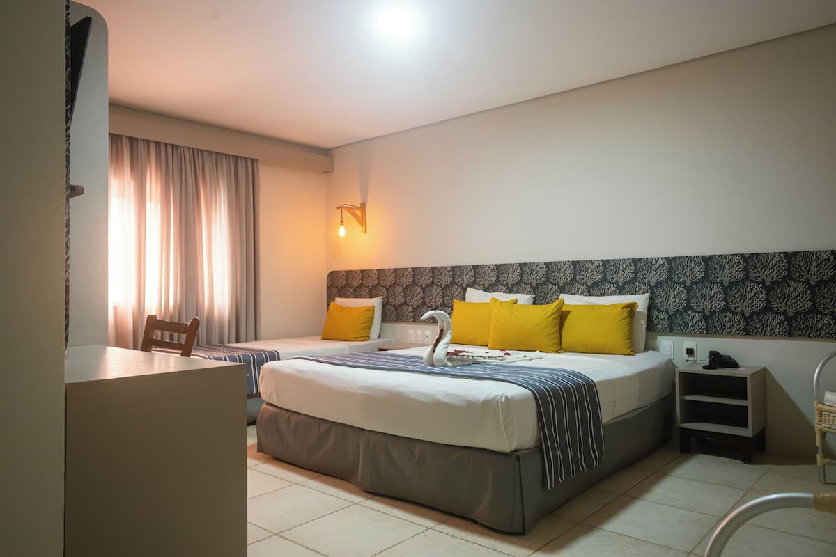 Habitación de hotel con dos camas, un escritorio, una silla, una mesita de noche y una lámpara en la pared.