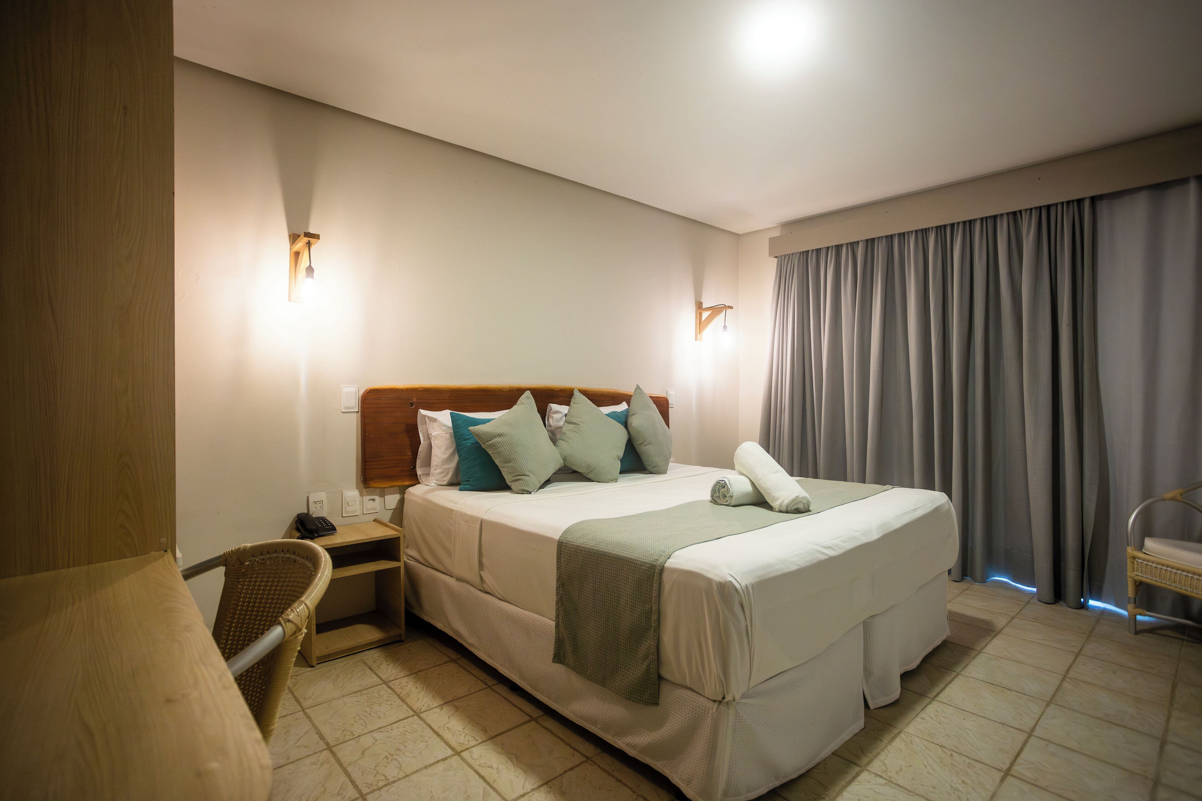 A hotel room with a bed, a nightstand, a chair, and a window with curtains.