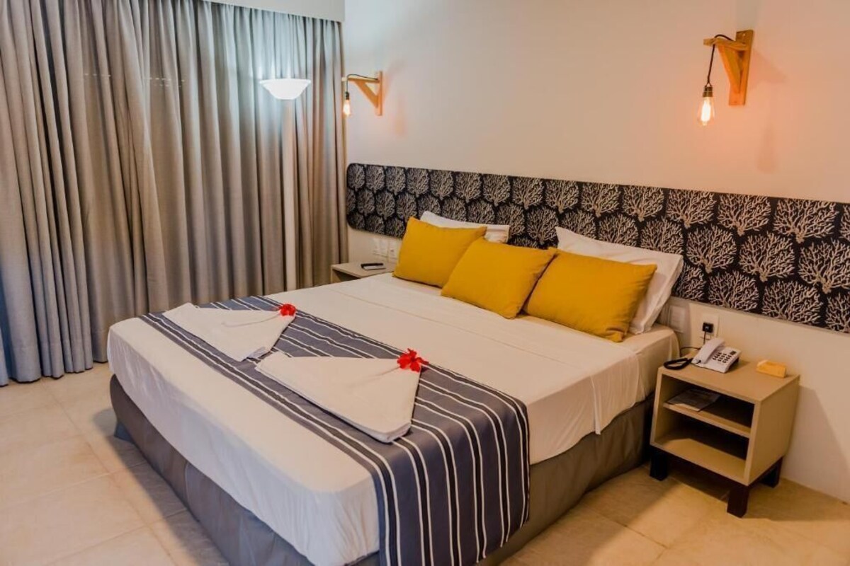 A hotel room with a large bed, two bedside tables, a telephone, and a wall-mounted light fixture.