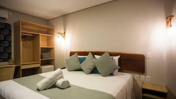 Een hotelkamer met een bed, een houten kledingkast, een nachtkastje en een wandlamp.