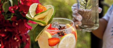 A person holding a glass with a cocktail garnished with lime, strawberry, and star anise. A bottle of Gordon's Gin is visible in the background.