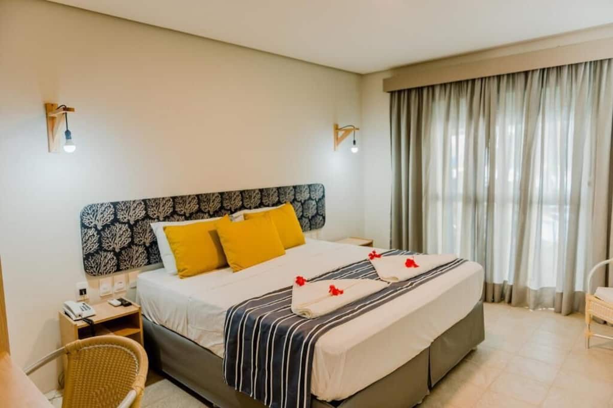 Una habitación de hotel con cama, mesita de noche, una silla y una ventana con cortinas.