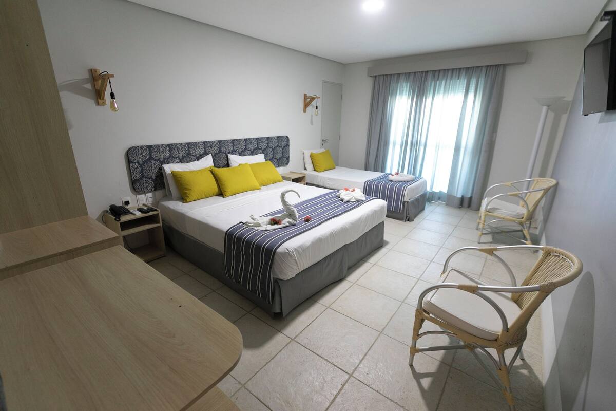Una habitación de hotel con dos camas, una mesa de madera y dos sillas de mimbre.