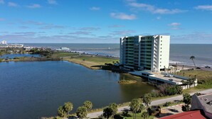 A high-rise hotel with multiple balconies, a parking area, and a view of the ocean.