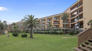 A multi-story hotel with balconies, a grassy courtyard, and palm trees.