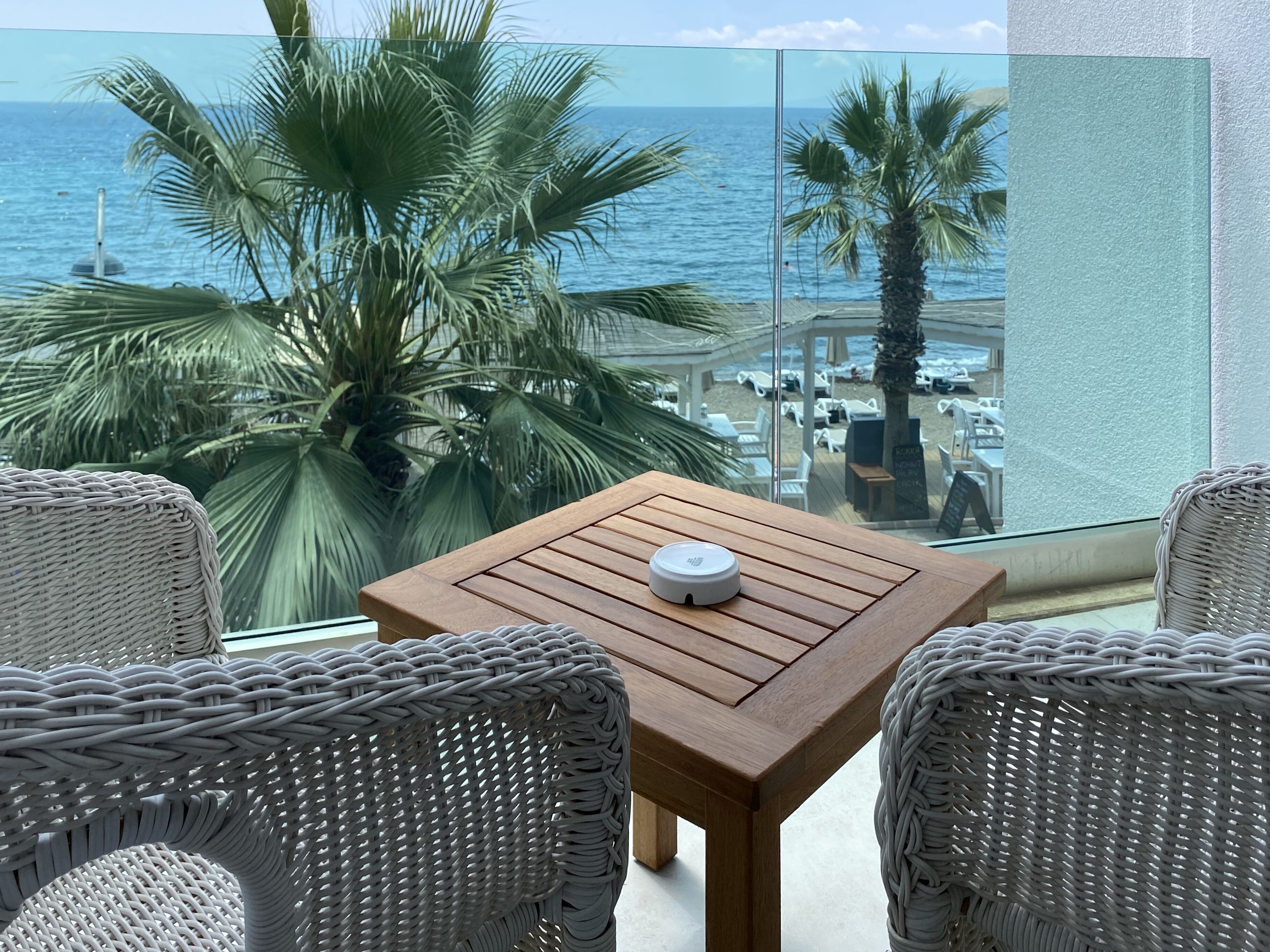 Un balcon agrémenté de meubles en osier, d’une table en bois et offrant une vue sur la plage et l’océan.