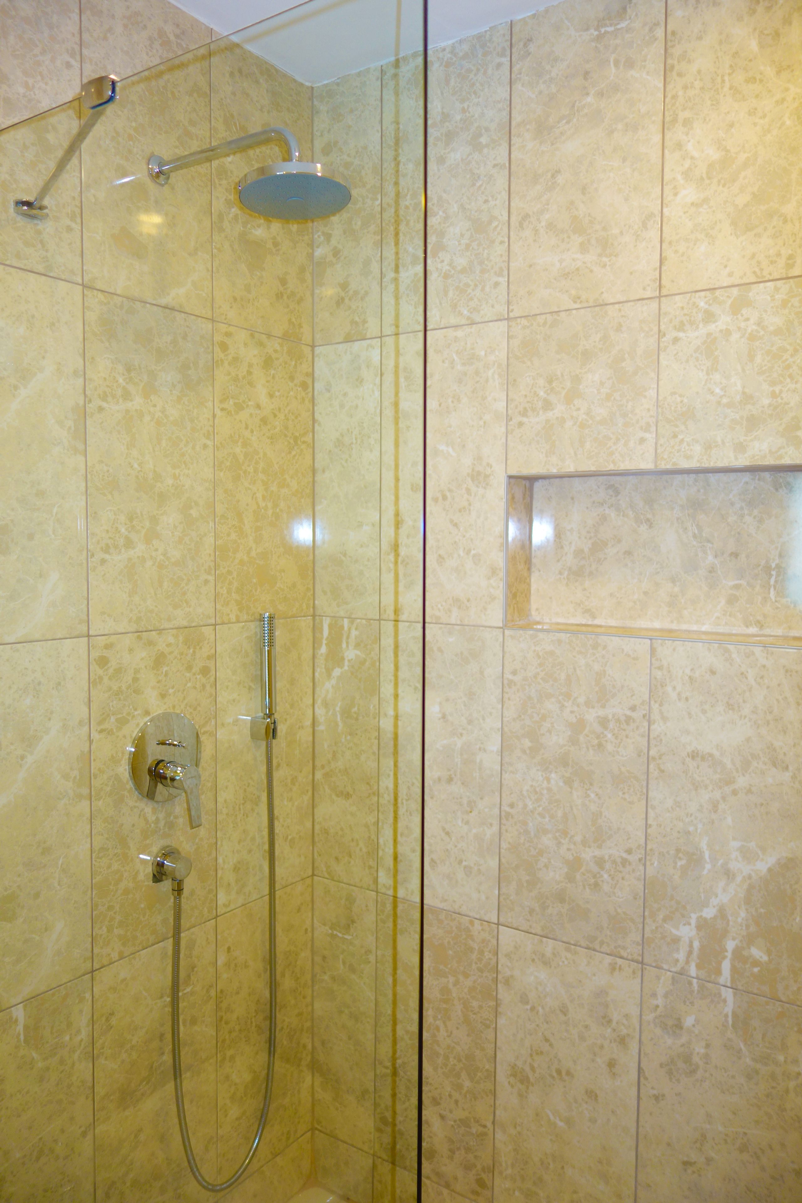 A shower with a handheld showerhead and a wall-mounted control.