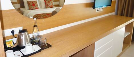 Habitación de hotel con mostrador de madera, un espejo que refleja la cama, un televisor montado en la pared y una cafetera sobre el mostrador.