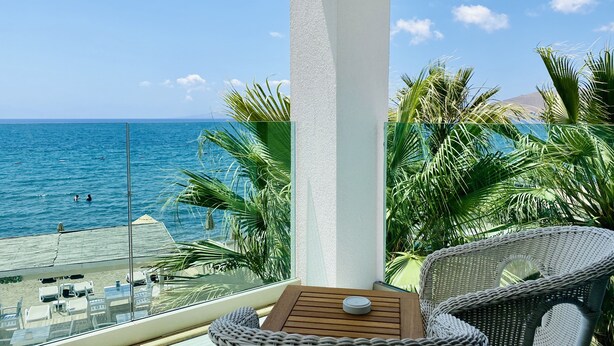 Un balcon avec vue sur la mer, une chaise en osier, une petite table et une rambarde en verre.