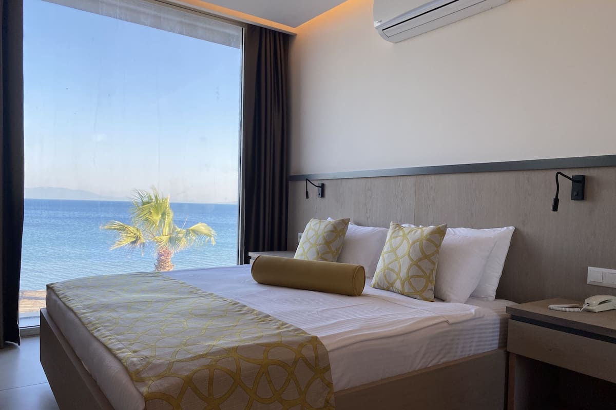 Habitación de hotel con una cama grande, una mesita de noche con teléfono y vista al mar.