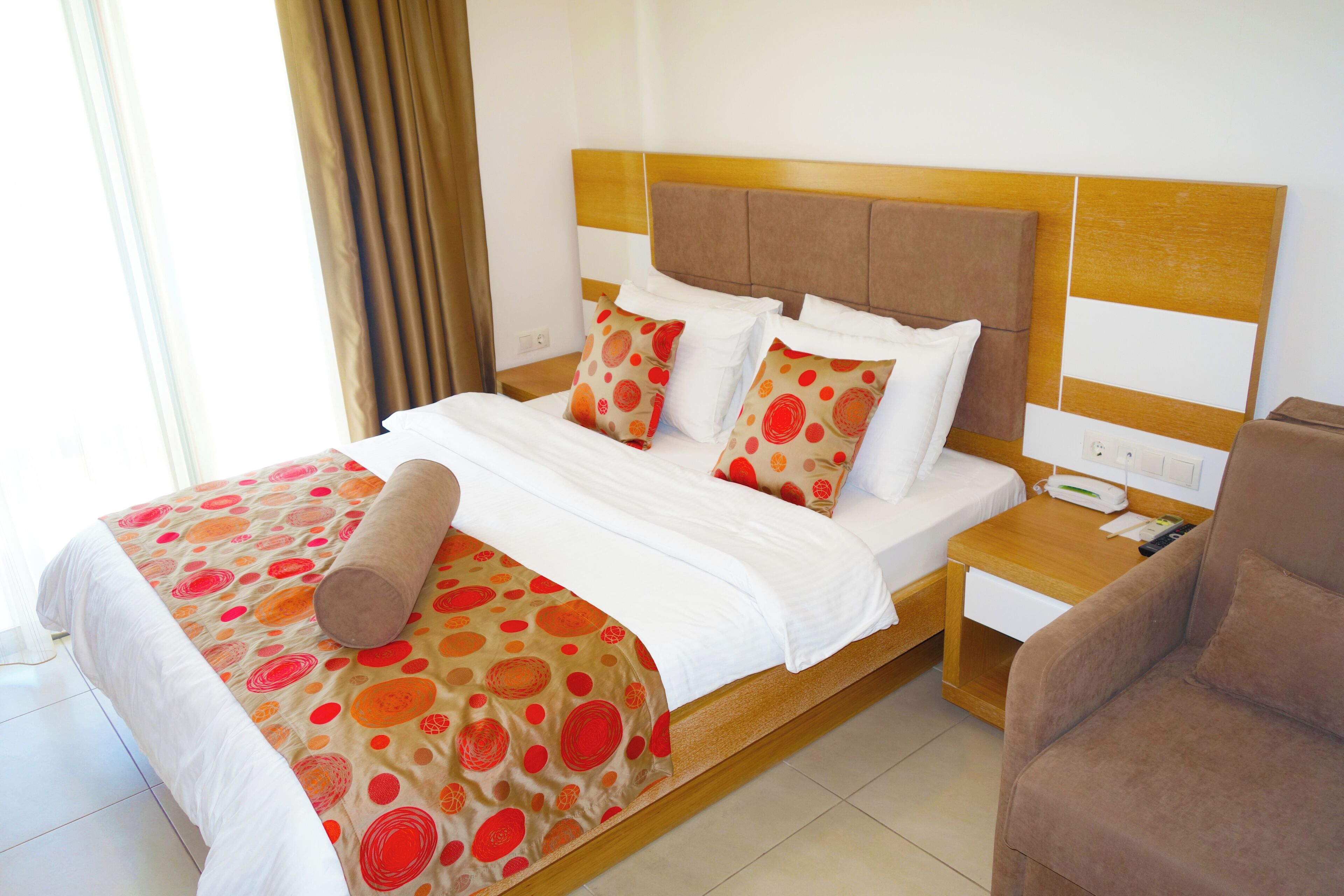 A neatly made bed with a patterned bedspread, a wooden headboard, a bedside table with a phone, and a chair.
