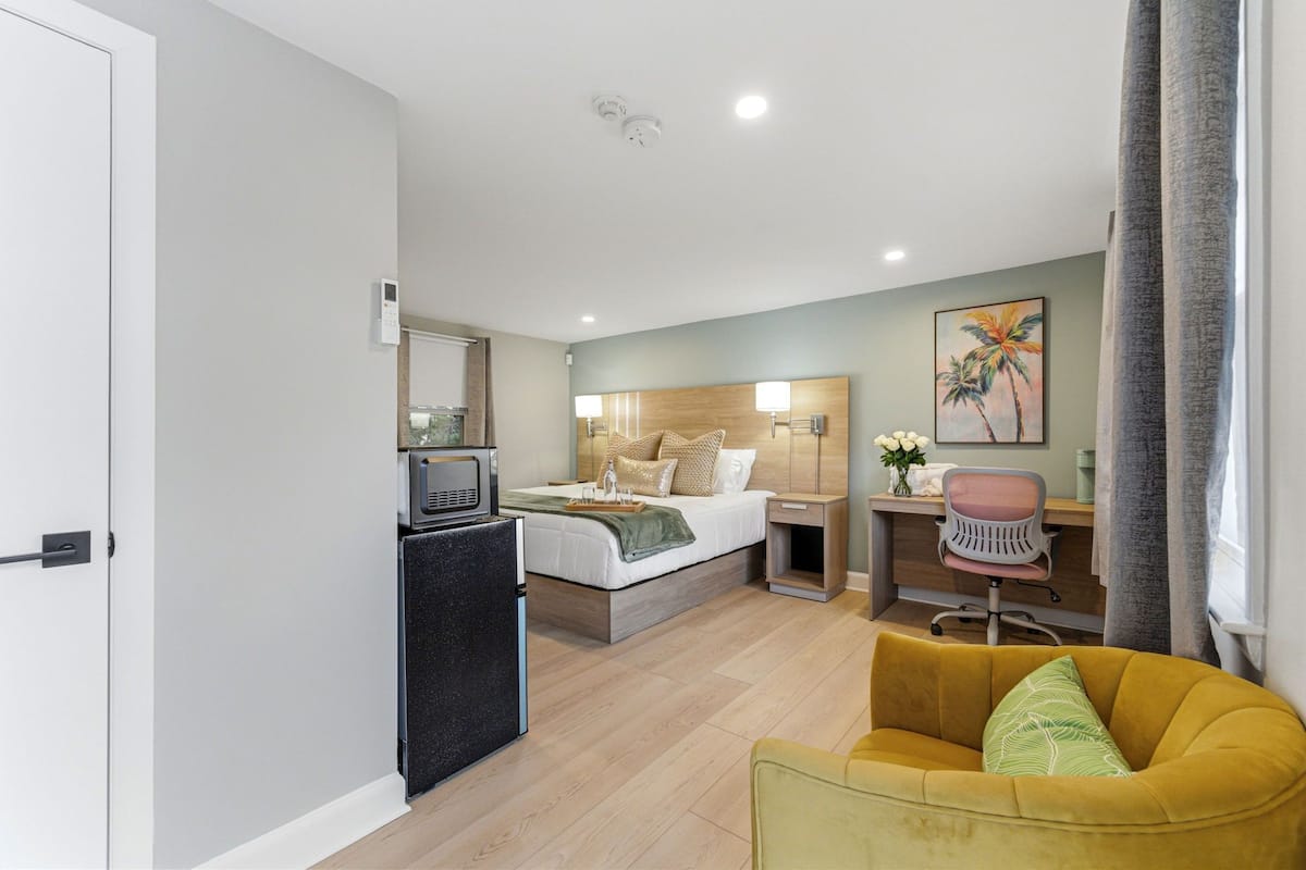 Habitación de hotel con cama, escritorio, silla y una pequeña kitchenette.