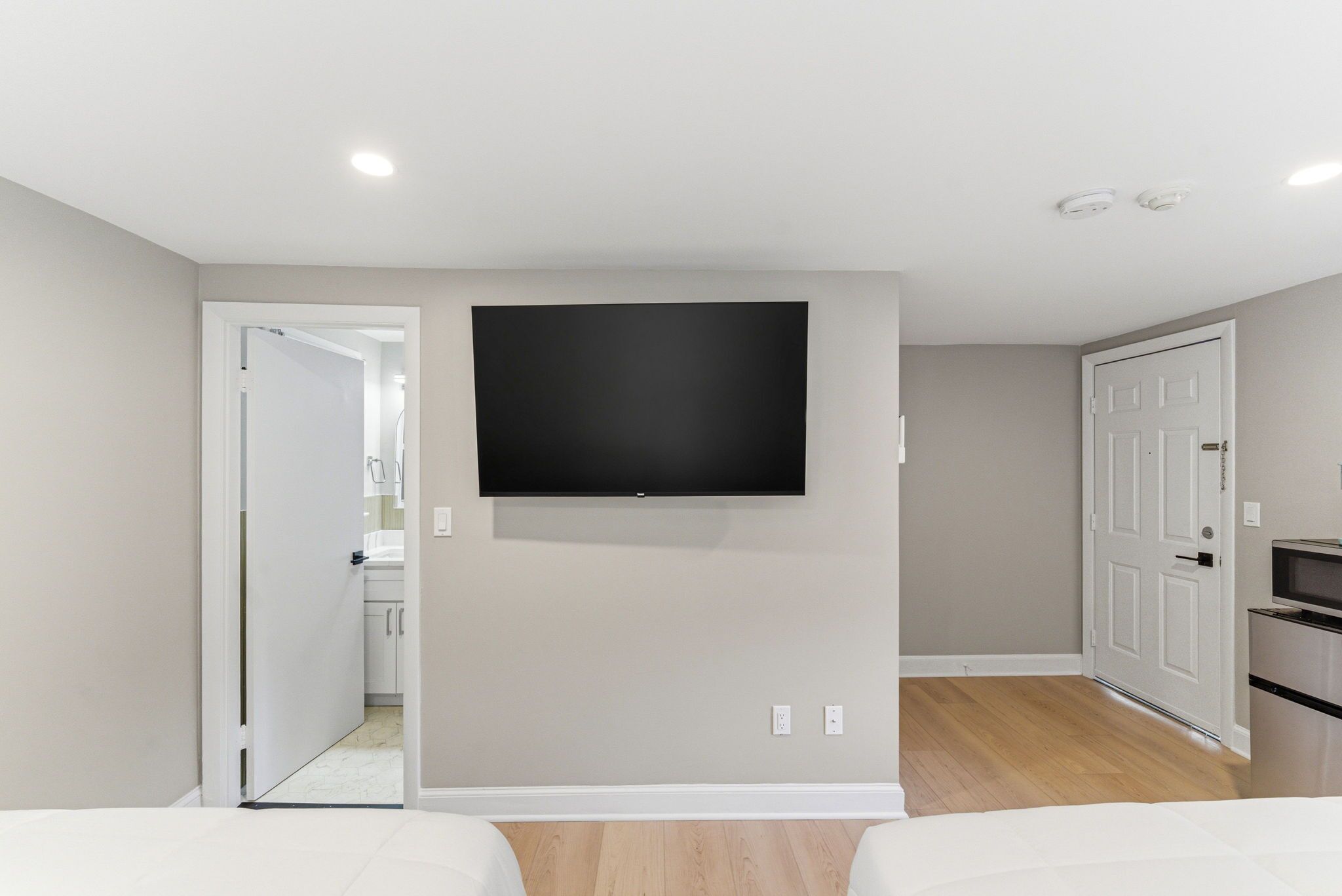 A bedroom with a bed, a TV mounted on the wall, and a door leading to a bathroom.