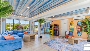 A modern living room with a blue sofa, a coffee table, a large window, and a surfboard decoration. - Dennis Port Surf Club (Boutique Hotel) (Dennis Port)