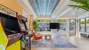 A room with arcade games, a TV, a large window, and a plant. - Dennis Port Surf Club (Boutique Hotel) (Dennis Port)