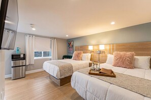 A hotel room with two beds, a microwave, a refrigerator, a window with curtains, and a painting on the wall.
