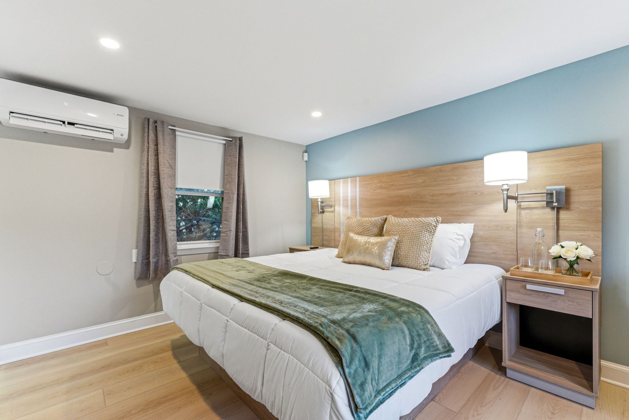 A modern hotel room with a large bed, a bedside table with a lamp, and an air conditioning unit on the wall.