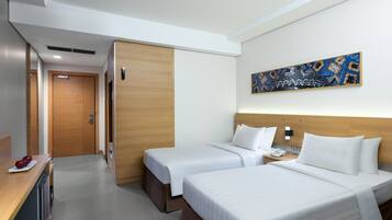 A hotel room with two beds, a wooden wardrobe, a desk with a telephone, and a painting on the wall.