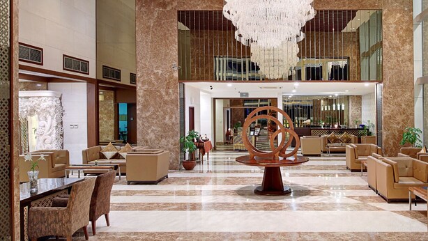 A spacious lobby with a large chandelier, seating areas, and a reception desk. - Aston Solo (Surakarta)