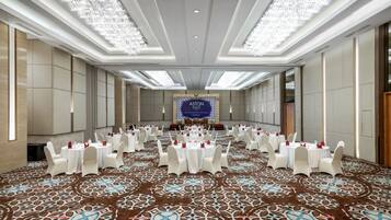 A spacious conference room with round tables, white chairs, and a patterned carpet.