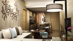 A modern living room with a sofa, a coffee table, and a dining area with a table and chairs. There is a decorative wall piece and a hanging light fixture. - Aston Solo (Surakarta)