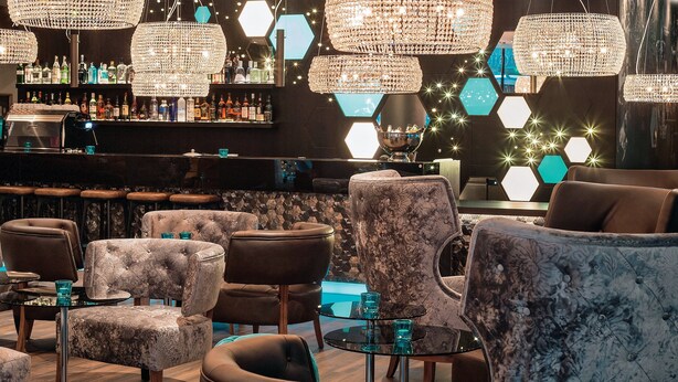 A bar area with multiple seating options, including sofas and armchairs, and a bar counter with various bottles. - Motel One London-Tower Hill (London)