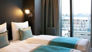 A hotel room with a large window, a bed with white and teal bedding, and a wall-mounted light. - Motel One London-Tower Hill (London)