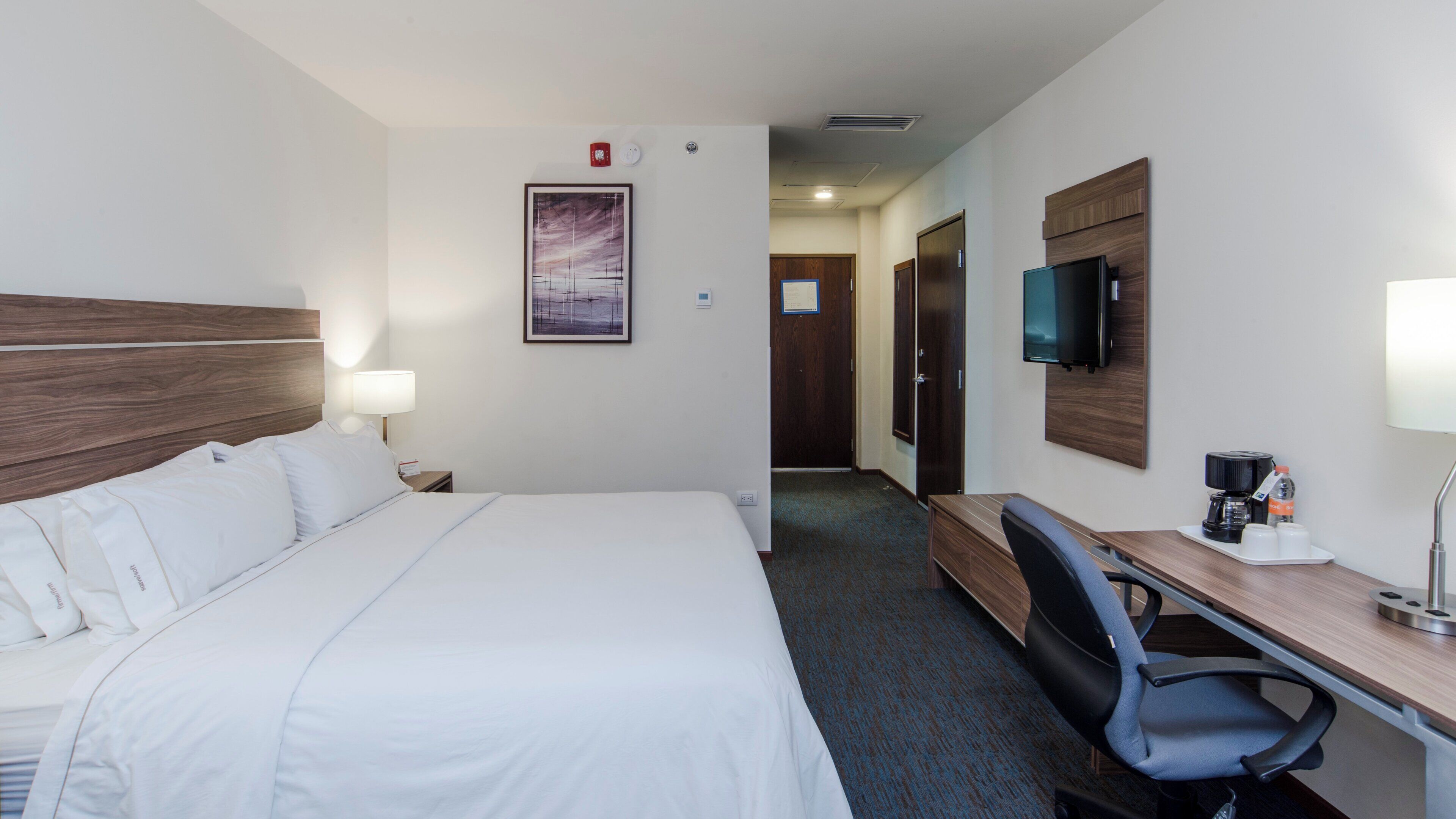 Habitación de hotel con cama, escritorio, silla, televisor y un cuadro en la pared.
