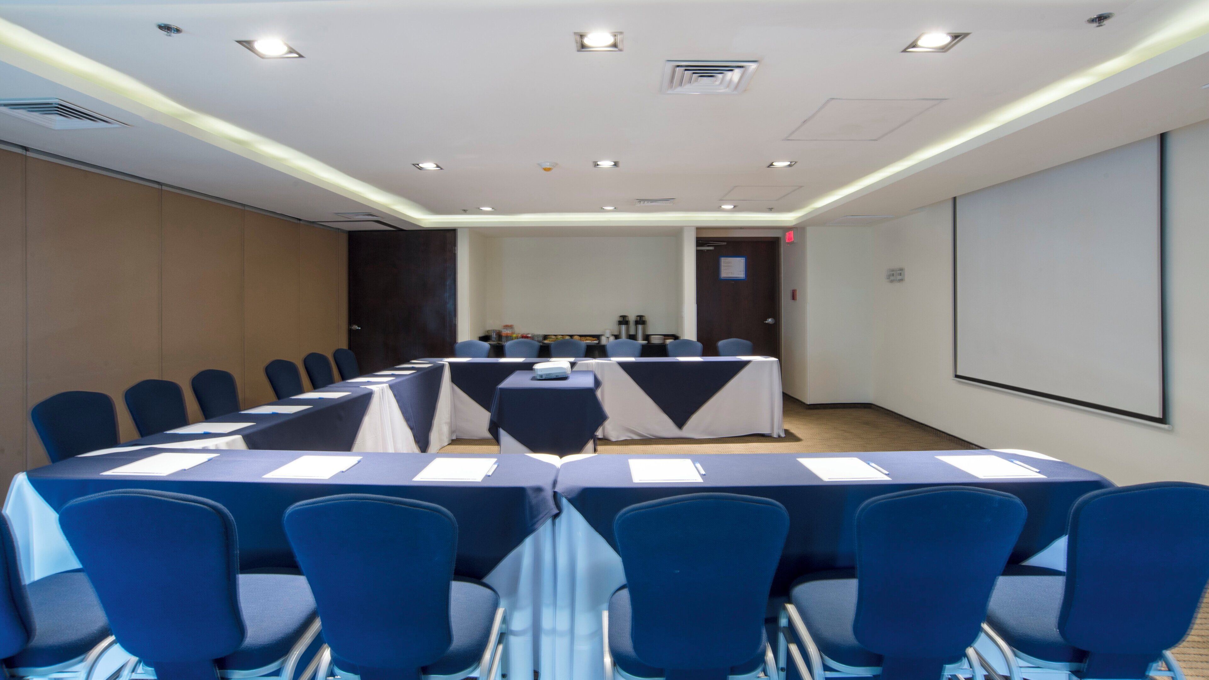 A conference room with a long table, chairs, a projector screen, and a whiteboard.