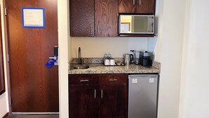 A compact kitchen with dark wood cabinets, a stainless steel refrigerator, a microwave, a coffee maker, and a toaster. - Holiday Inn Express Culiacan by IHG (Culiacán)