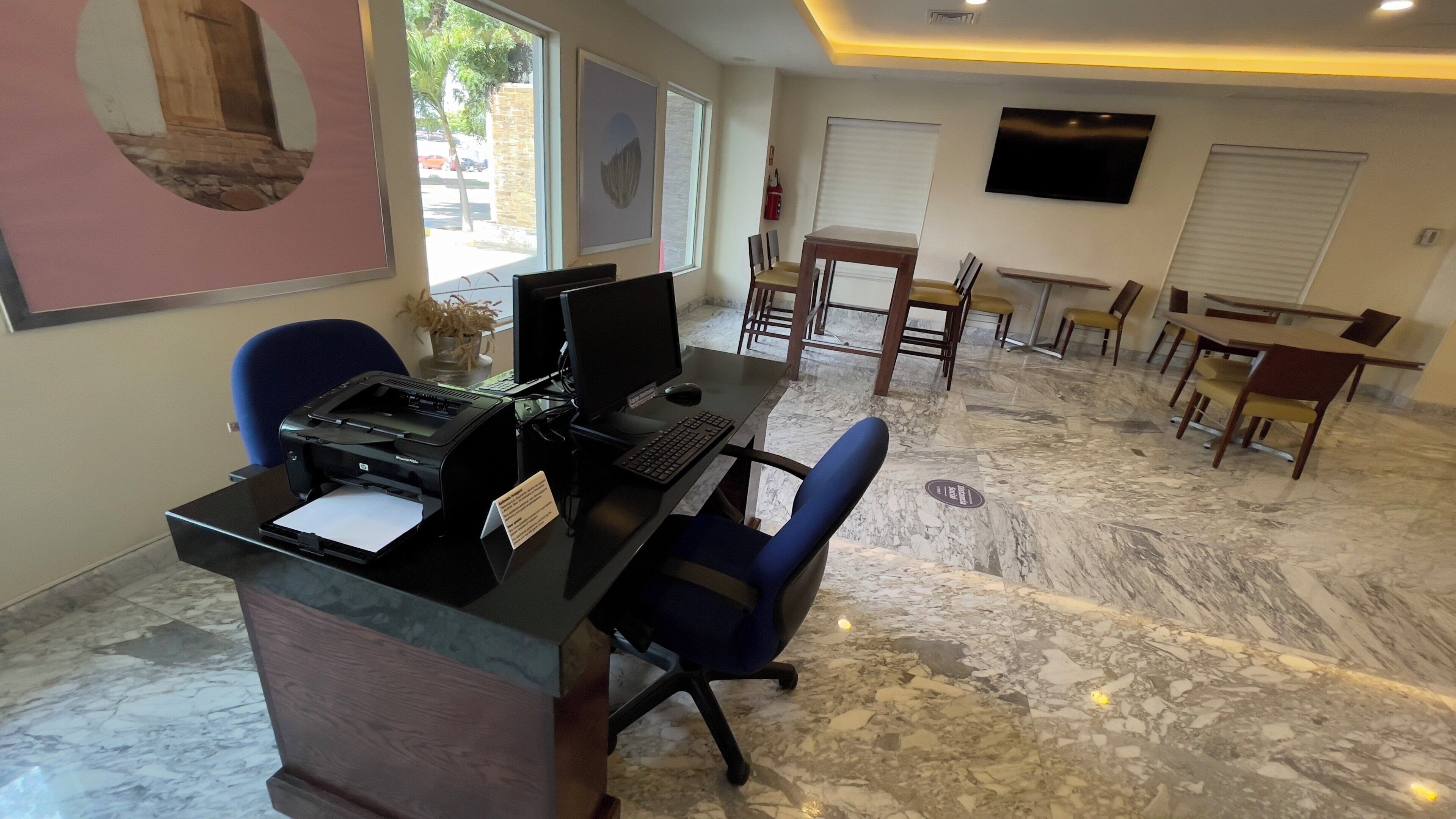 Uma área de recepção de hotel com balcão, computador, cadeiras e televisão.