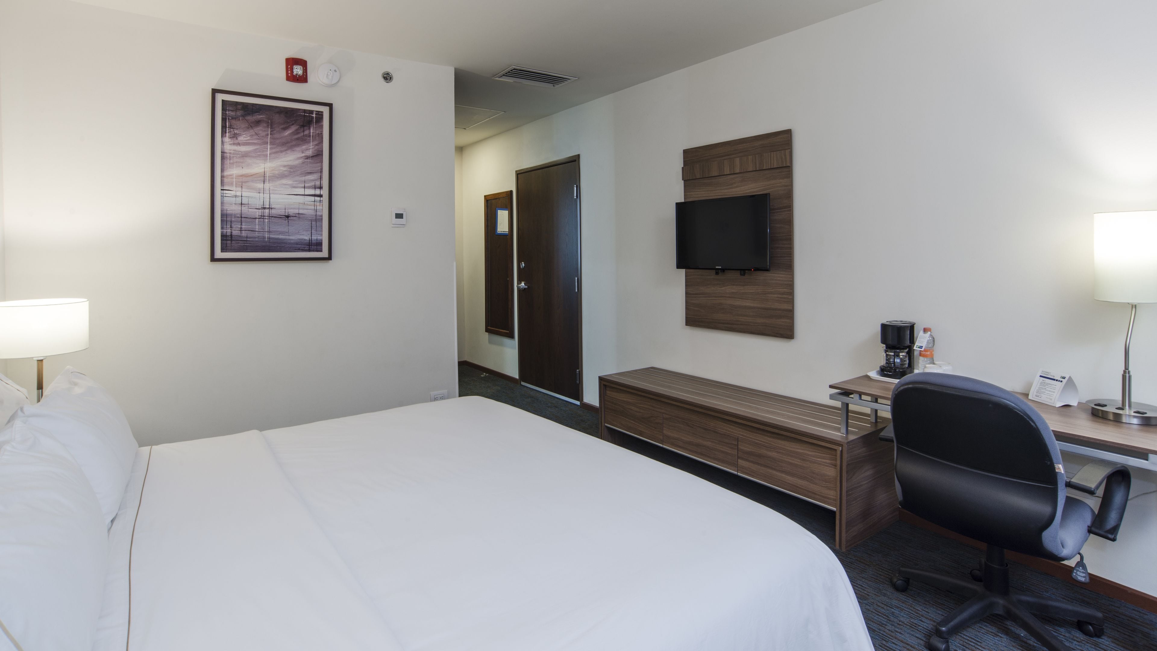 A hotel room with a large bed, a desk with a chair, a television, and a coffee maker.