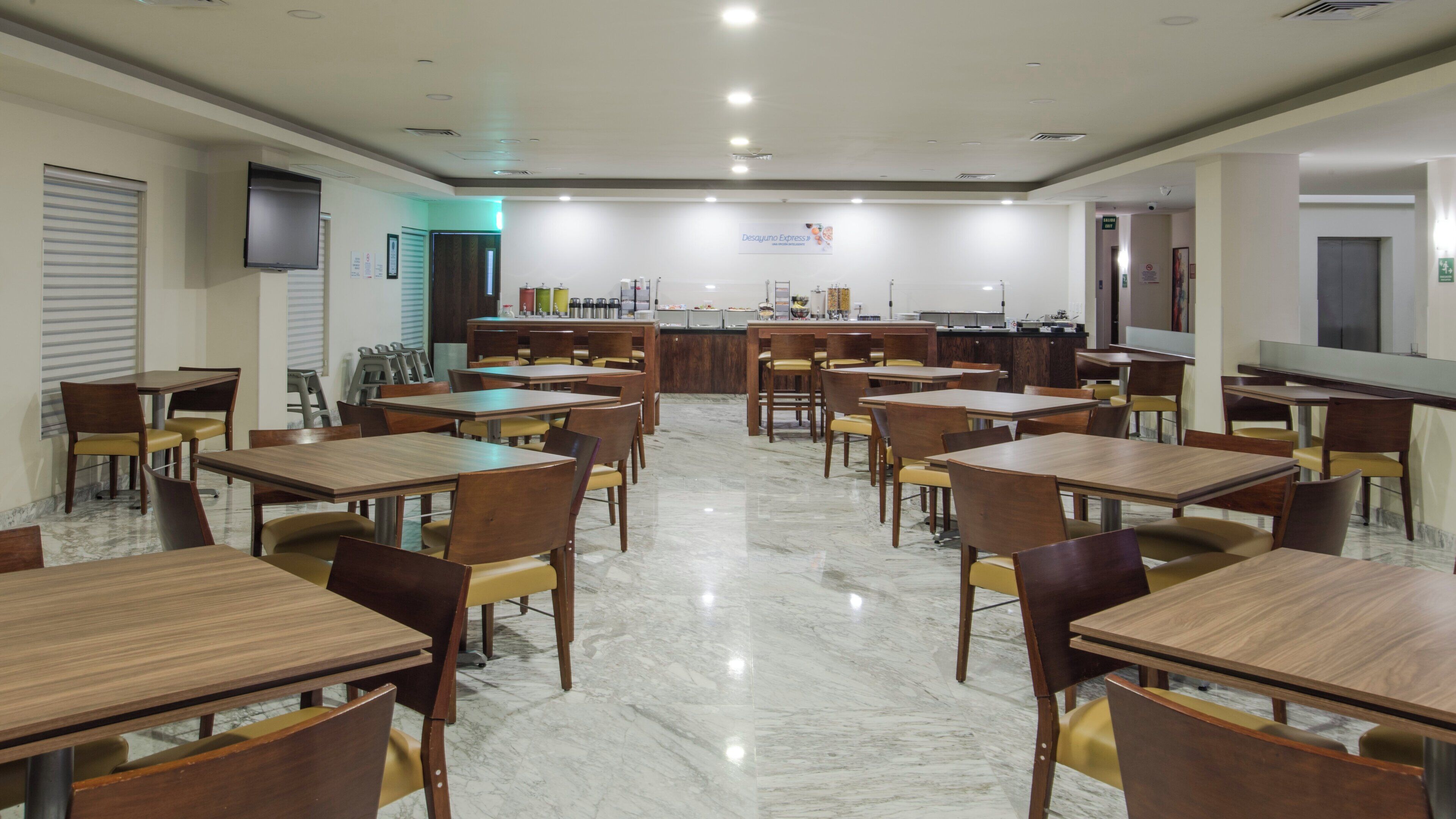 A spacious dining area with multiple tables and chairs, a counter with food and beverage options, and a television mounted on the wall.