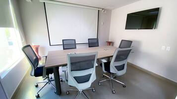 Ein Konferenzraum mit einem großen Tisch, sechs Stühlen, einer Projektionsleinwand und einem flachbildschirm-Fernseher an der Wand.