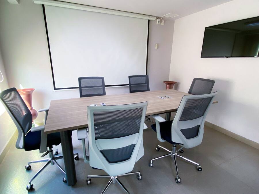 Ein Konferenzraum mit einem großen Tisch, sechs Stühlen, einer Projektionsleinwand und einem flachbildschirm-Fernseher an der Wand.